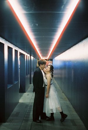 Couple sharing a romantic moment in a neon-lit corridor with red and blue lights creating a dramatic tunnel effect.
