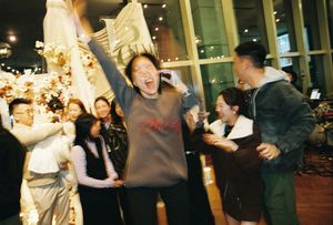 Joyful group of people celebrating at an indoor event, with a woman raising her arms in excitement.