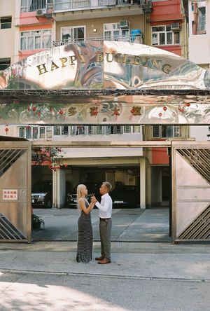 Couple holding hands in front of Happy Building sign in Hong Kong urban street setting.
