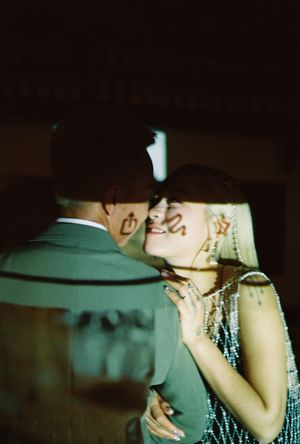 A couple in vintage attire share a romantic dance, the woman wearing a beaded dress and bold face paint.