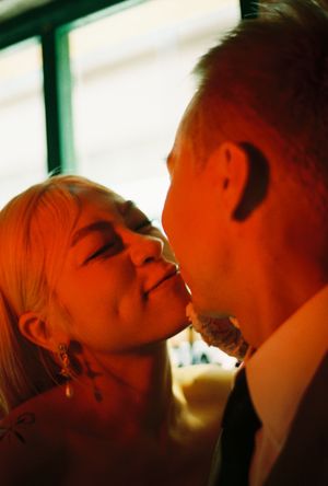 A couple shares a romantic kiss bathed in warm amber light, the woman with blonde hair and elegant earrings.