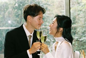 Couple in formal attire toasting with champagne glasses, smiling at each other at a wedding celebration.