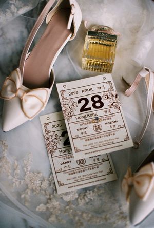 Elegant wedding flat lay featuring blush bow heels, perfume bottle, and a Hong Kong wedding invitation dated April 28, 2026.