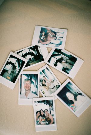 A scattered collection of Polaroid instant photos on a beige surface showing various candid moments and group shots.