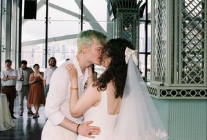 Newlyweds share their first kiss at wedding ceremony in elegant venue with guests applauding.
