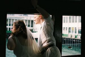Bride and groom sharing a romantic moment by a window on a ferry with waterfront views.