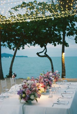 Elegant beachside wedding reception at dusk with string lights, floral centerpieces, and ocean views.