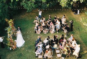 Aerial view of an outdoor garden wedding ceremony with guests seated around the bride and groom under string lights.