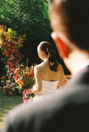 Bride holding colorful bouquet at outdoor garden wedding ceremony with vibrant floral backdrop.