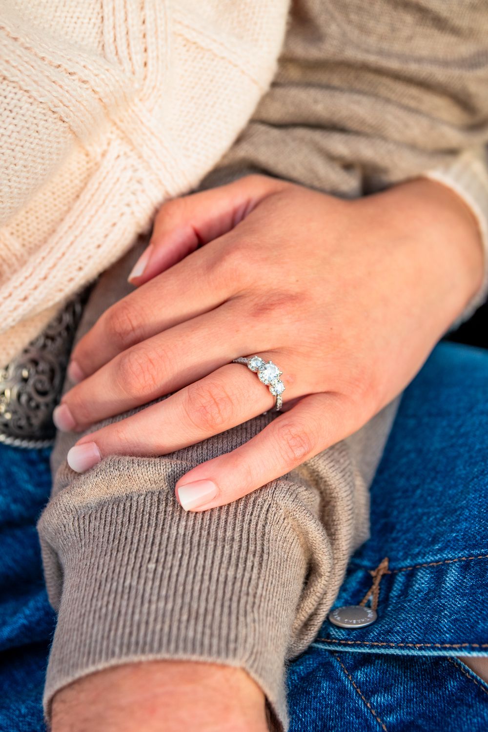 Close-up of a woman's hand wearing a three-stone diamond engagement ring resting on a man's arm.