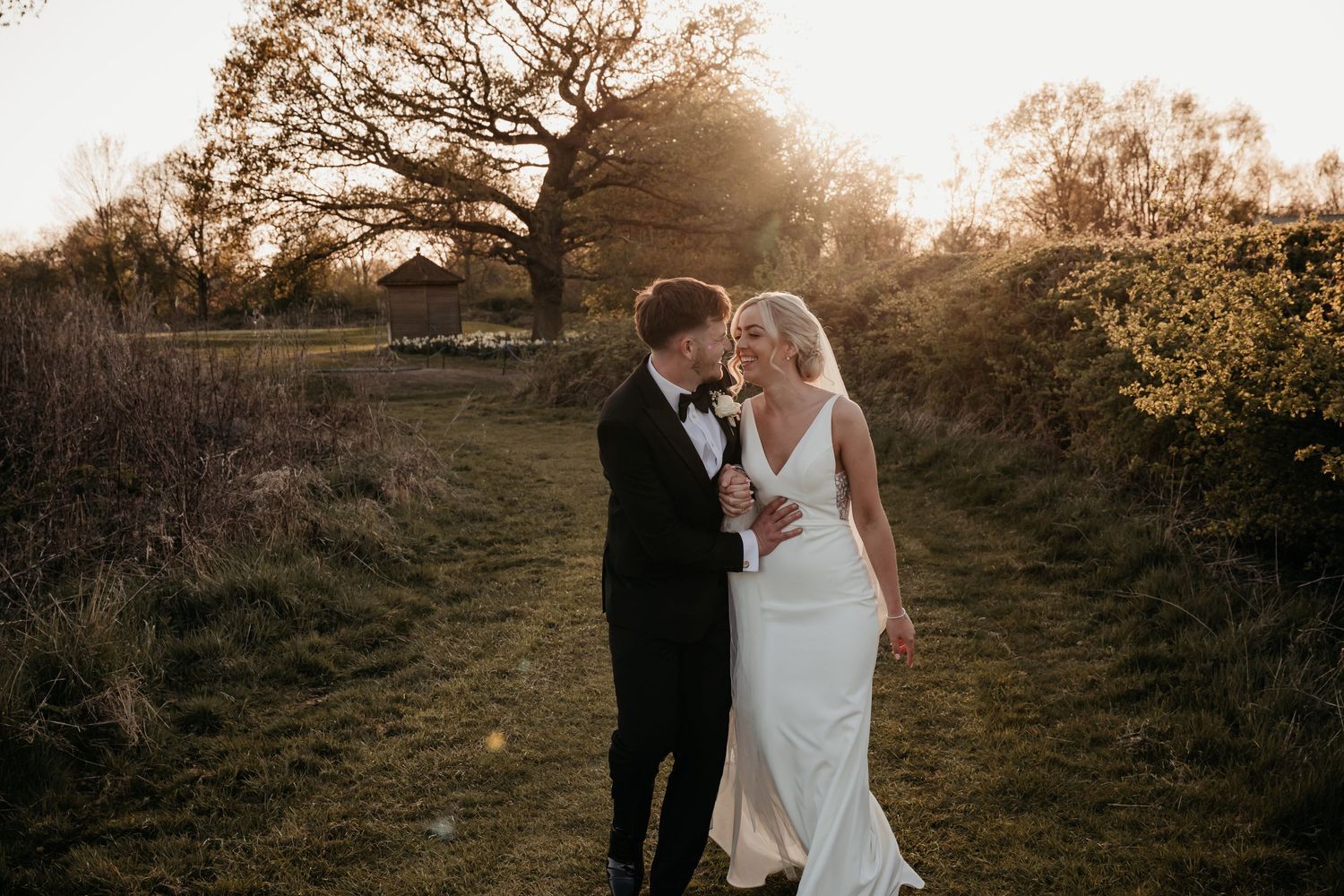 A bride and groom share a romantic moment at golden hour in a lush green countryside setting.