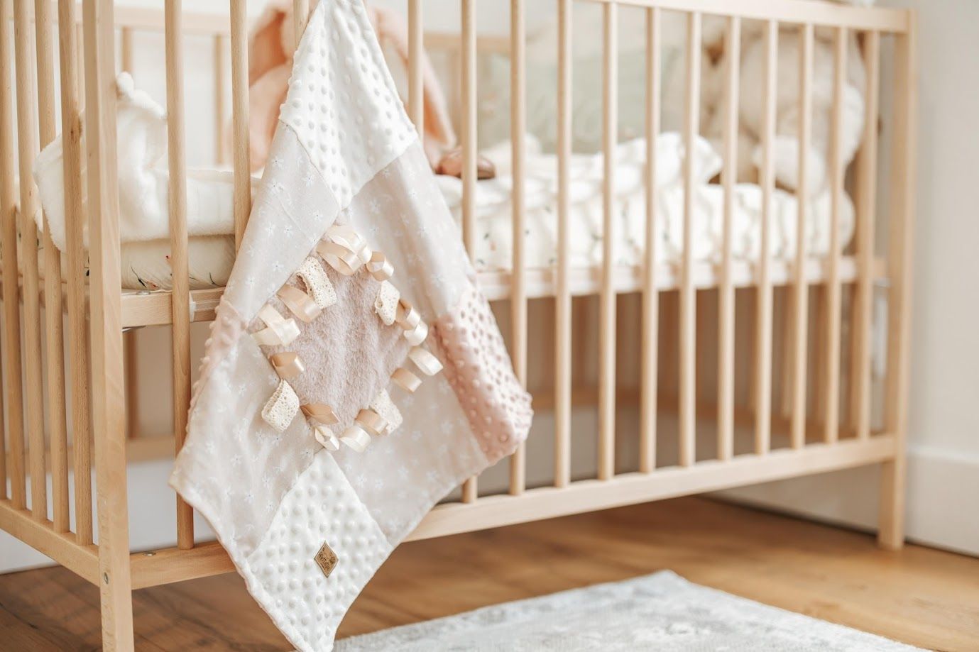 Handmade baby sensory blanket with giraffe print fabric squares, minky dot texture, and satin ribbon tags in neutral beige tones.