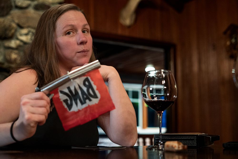 Woman holding a red bag with wine glass on wooden bar counter in a cozy rustic restaurant setting.