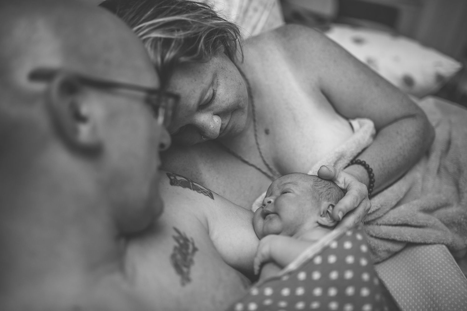 Newborn baby resting on parent's chest wrapped in a soft brown towel after birth.