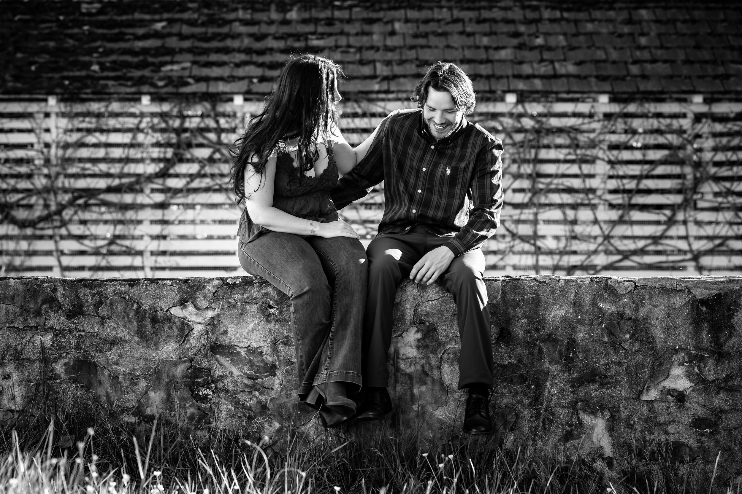 Black and white photo of two people sitting on a stone wall, sharing an intimate conversation outdoors.