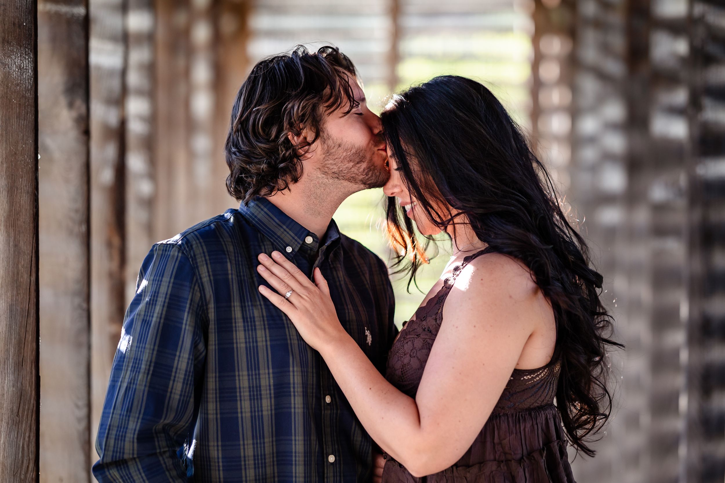 Romantic couple sharing a passionate kiss in a rustic wooden setting with warm natural lighting.