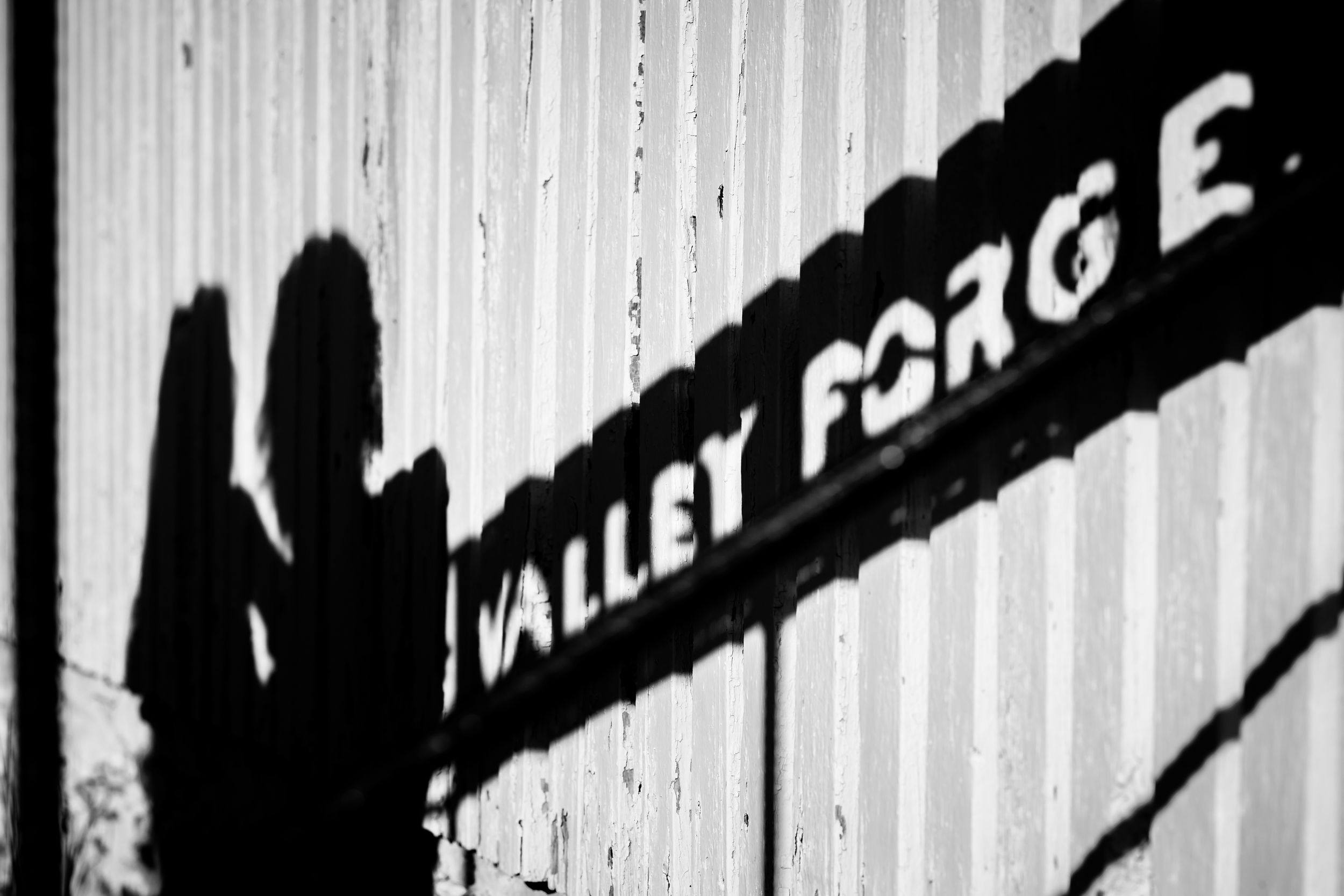 Black and white photo of a Valley Forge sign casting a shadow on a corrugated metal wall.
