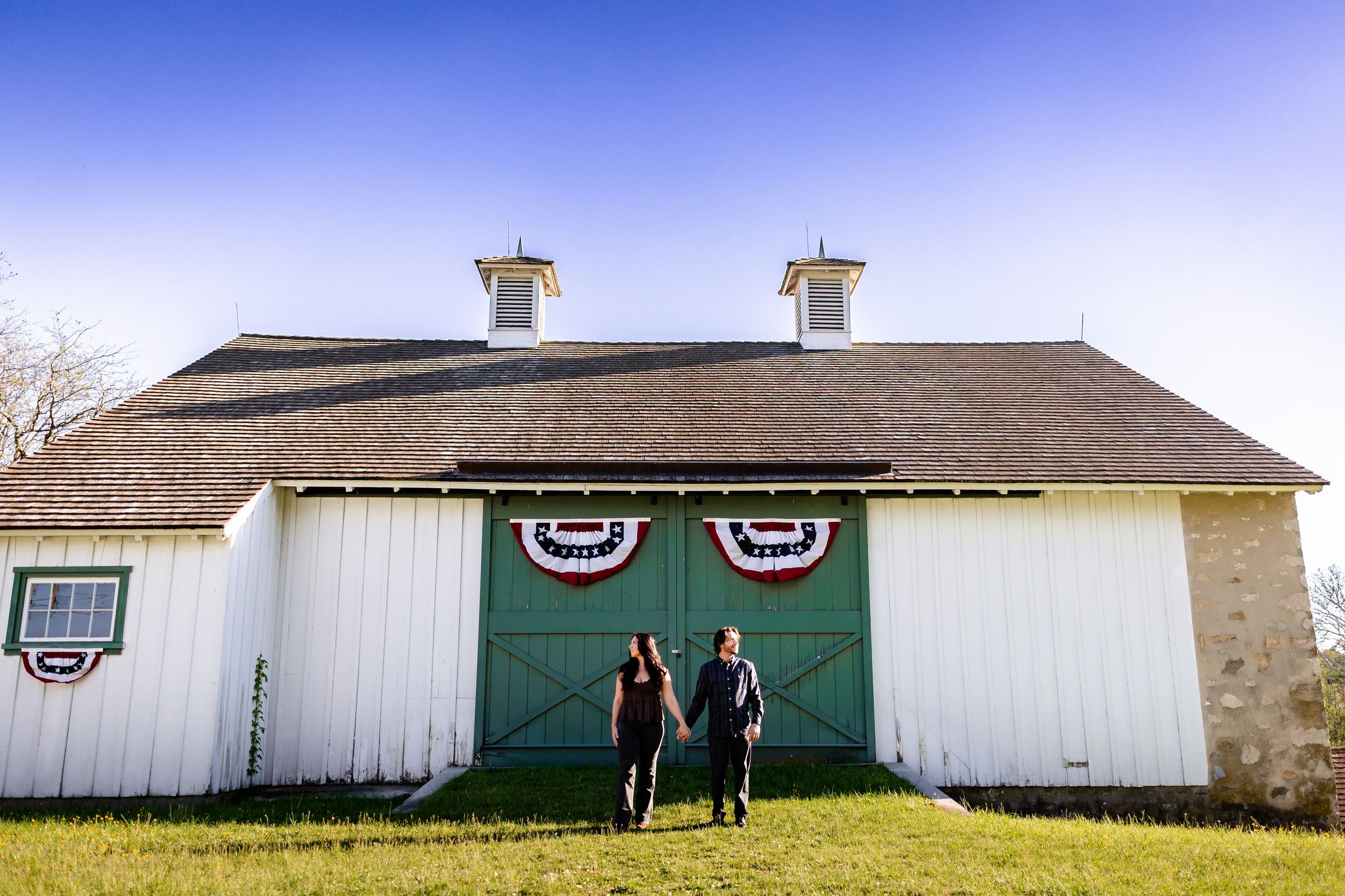 Couple walking in front of a white barn with green doors and patriotic bunting decorations.