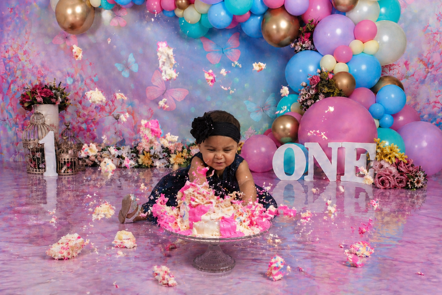 Baby's first birthday cake smash with pink floral cake, balloon arch, and ONE letters in colorful party setting.