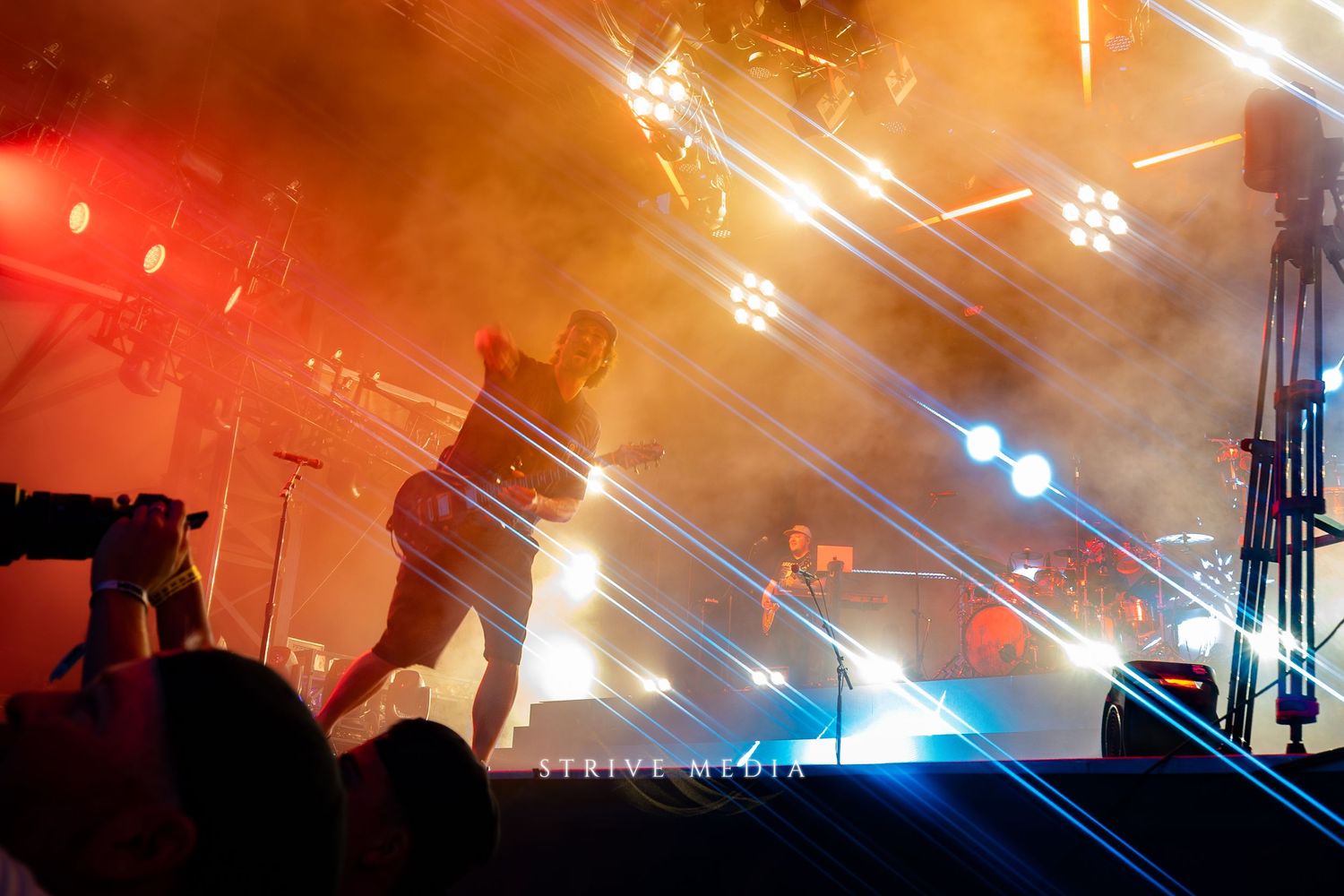 Performer on stage surrounded by colorful laser lights and fog at an energetic live concert.