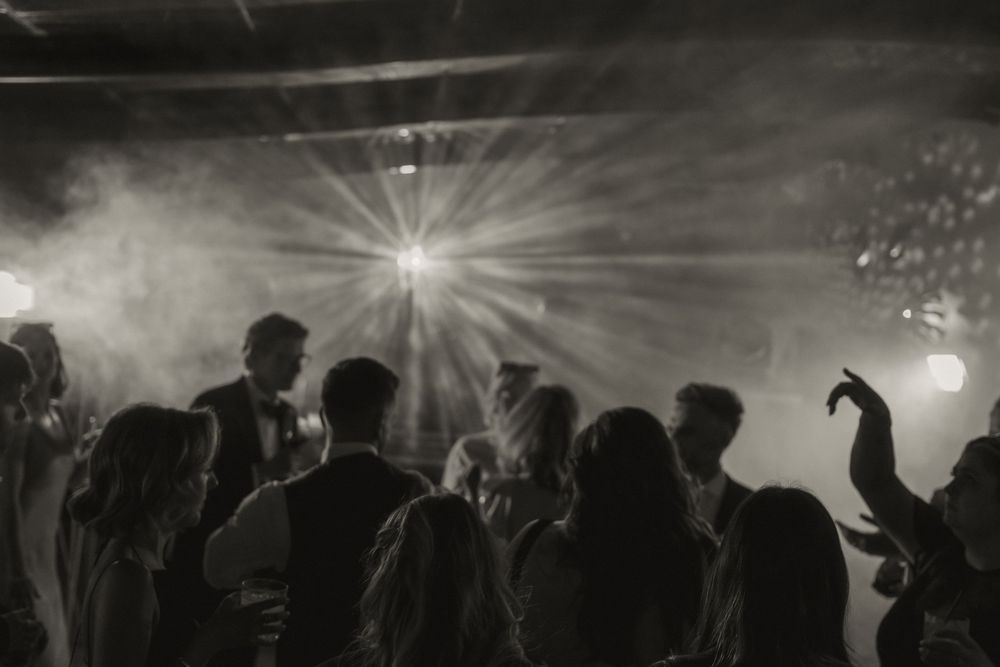 Black and white photo of silhouetted dancers at a party with dramatic light beams and fog effects.