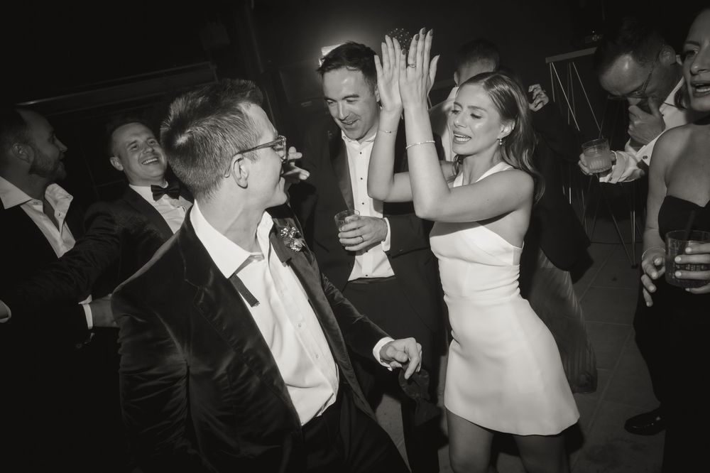 Black and white photo of guests high-fiving and dancing joyfully at an elegant wedding reception party.