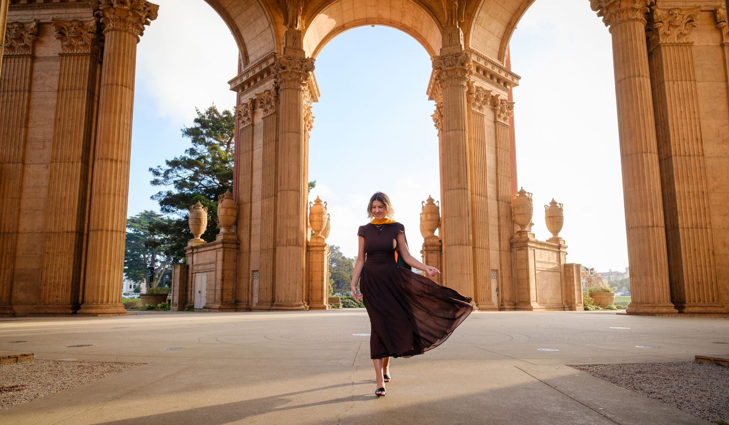 Woman in black dress walking under grand stone arches at the Palace of Fine Arts, San Francisco.