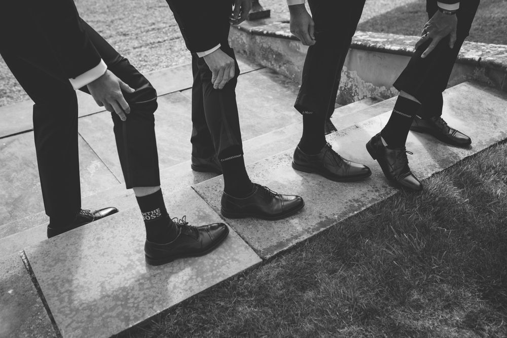Close-up black and white photo of groomsmen showing off their dress shoes and socks at a wedding.