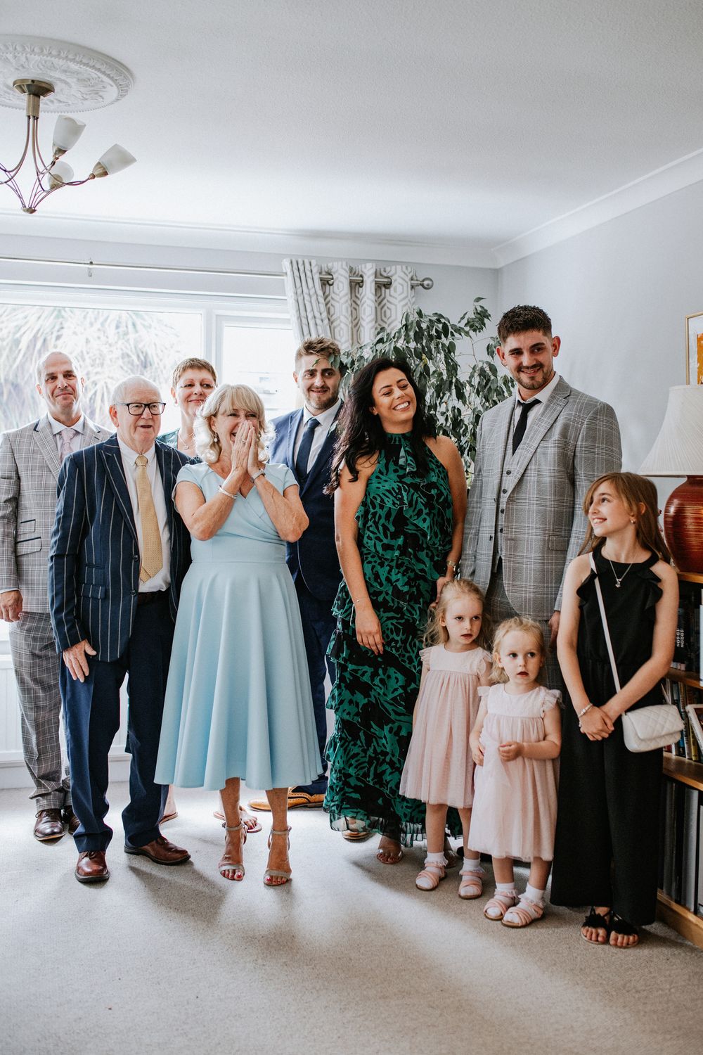 Family group photo at a wedding celebration, gathered indoors with joyful expressions, dressed in formal attire.