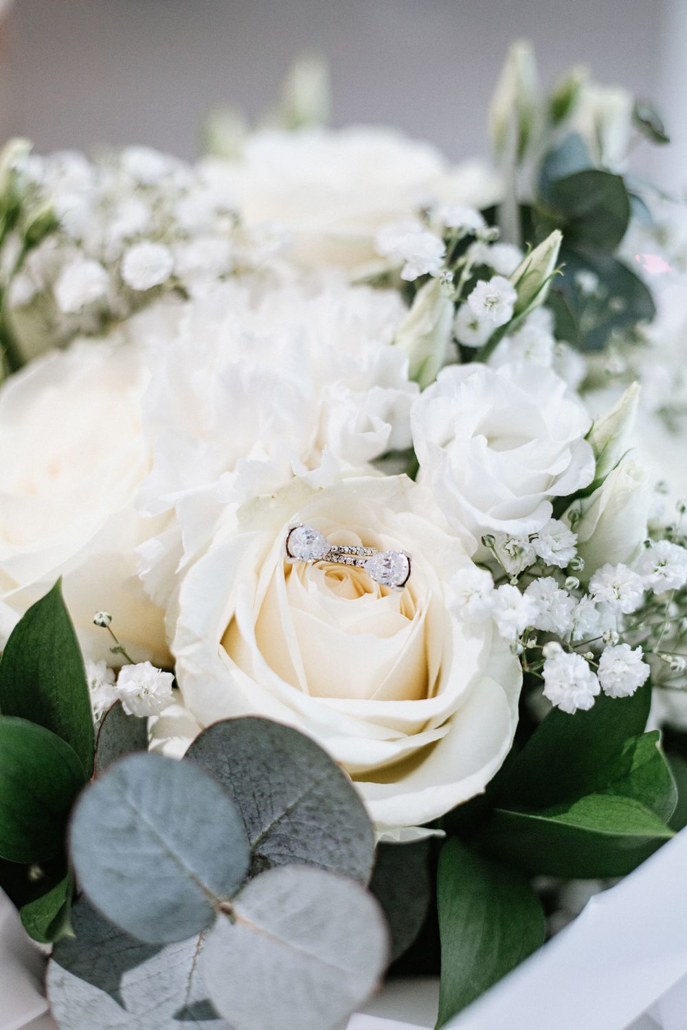 Wedding rings nestled in white roses and eucalyptus bridal bouquet with baby's breath.