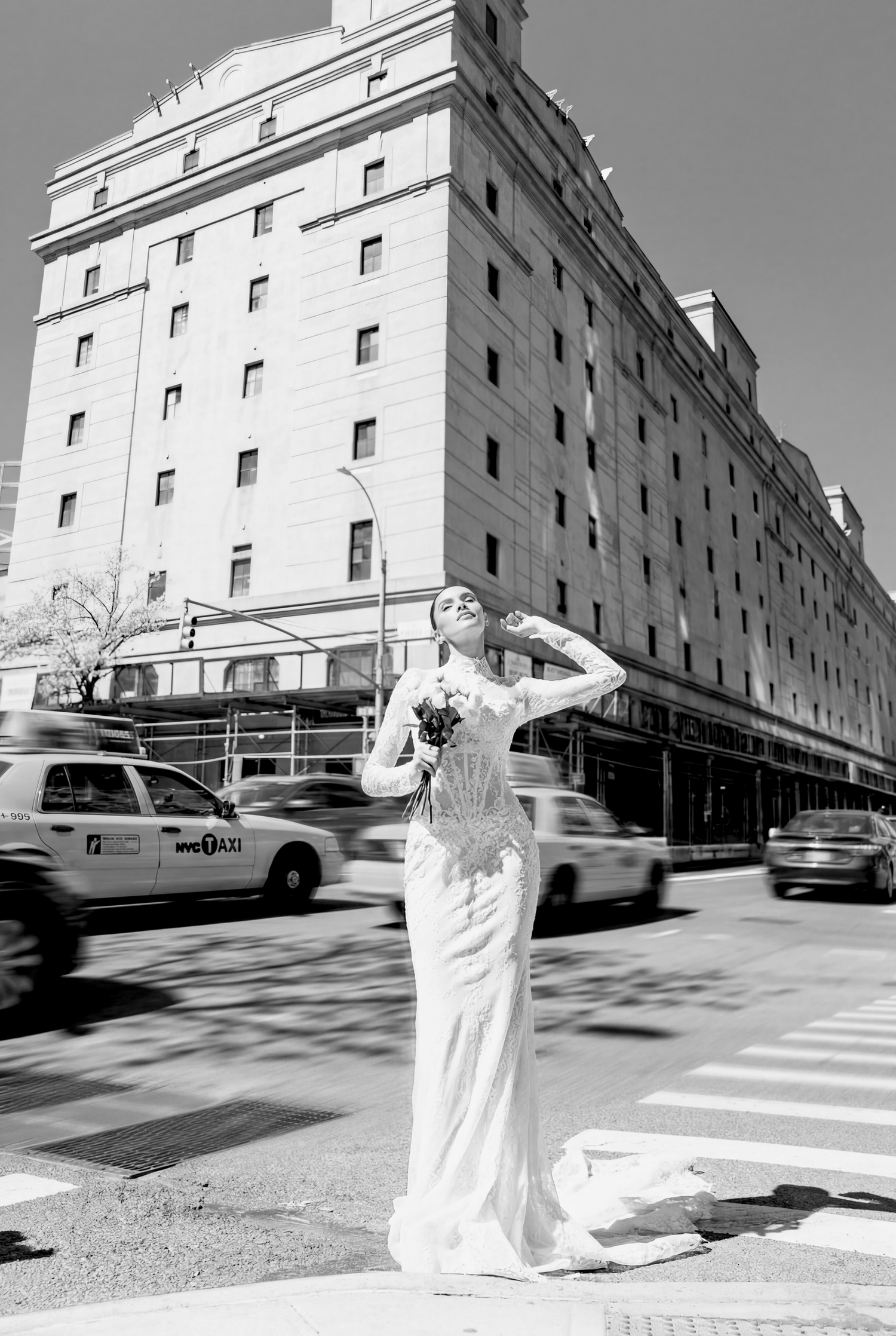 Bride in white gown hailing a taxi on a New York City street, with yellow cabs and a grand hotel in the background.