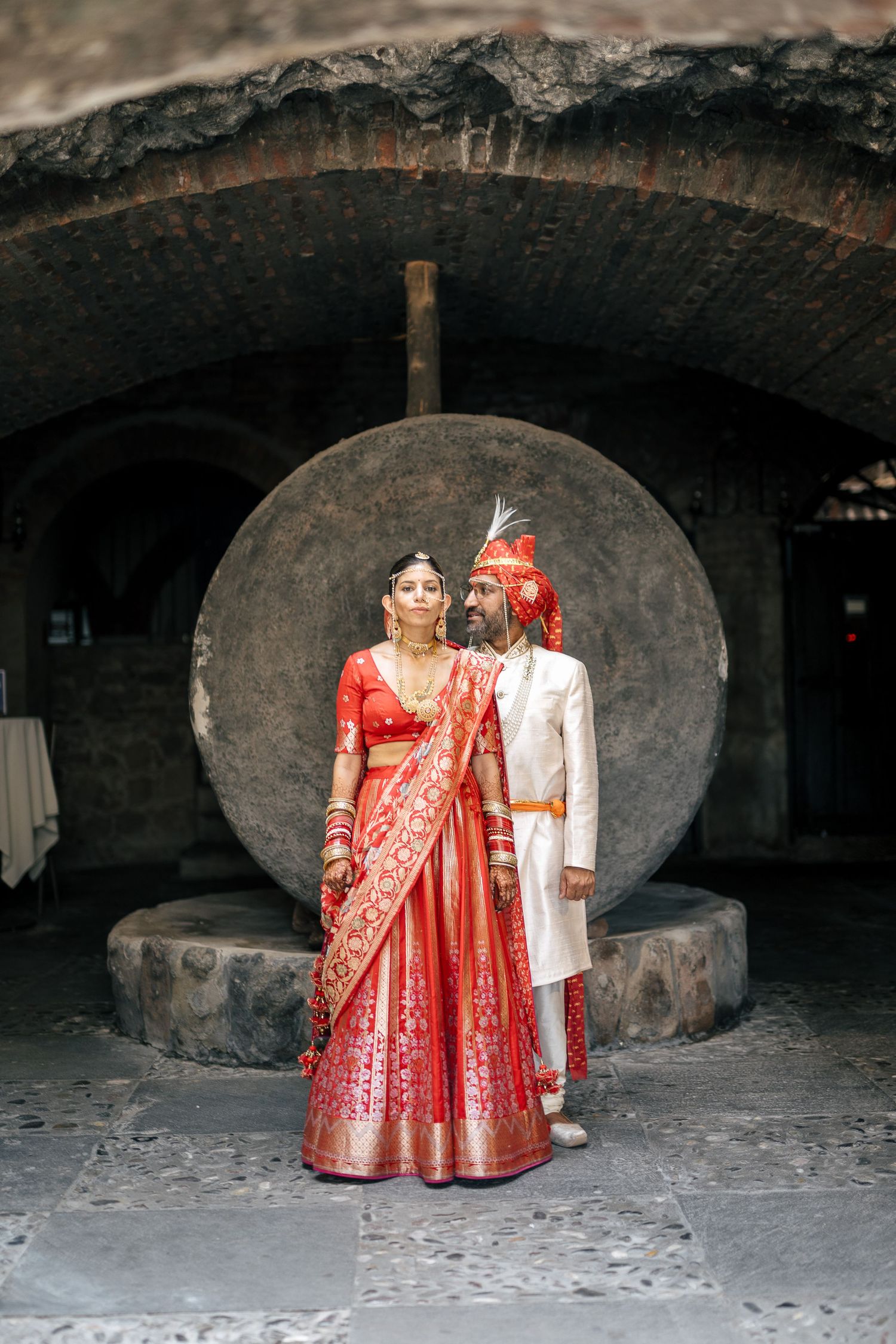 Indian couple in yellow outfits celebrate Haldi ceremony under stone archway adorned with marigold flowers.