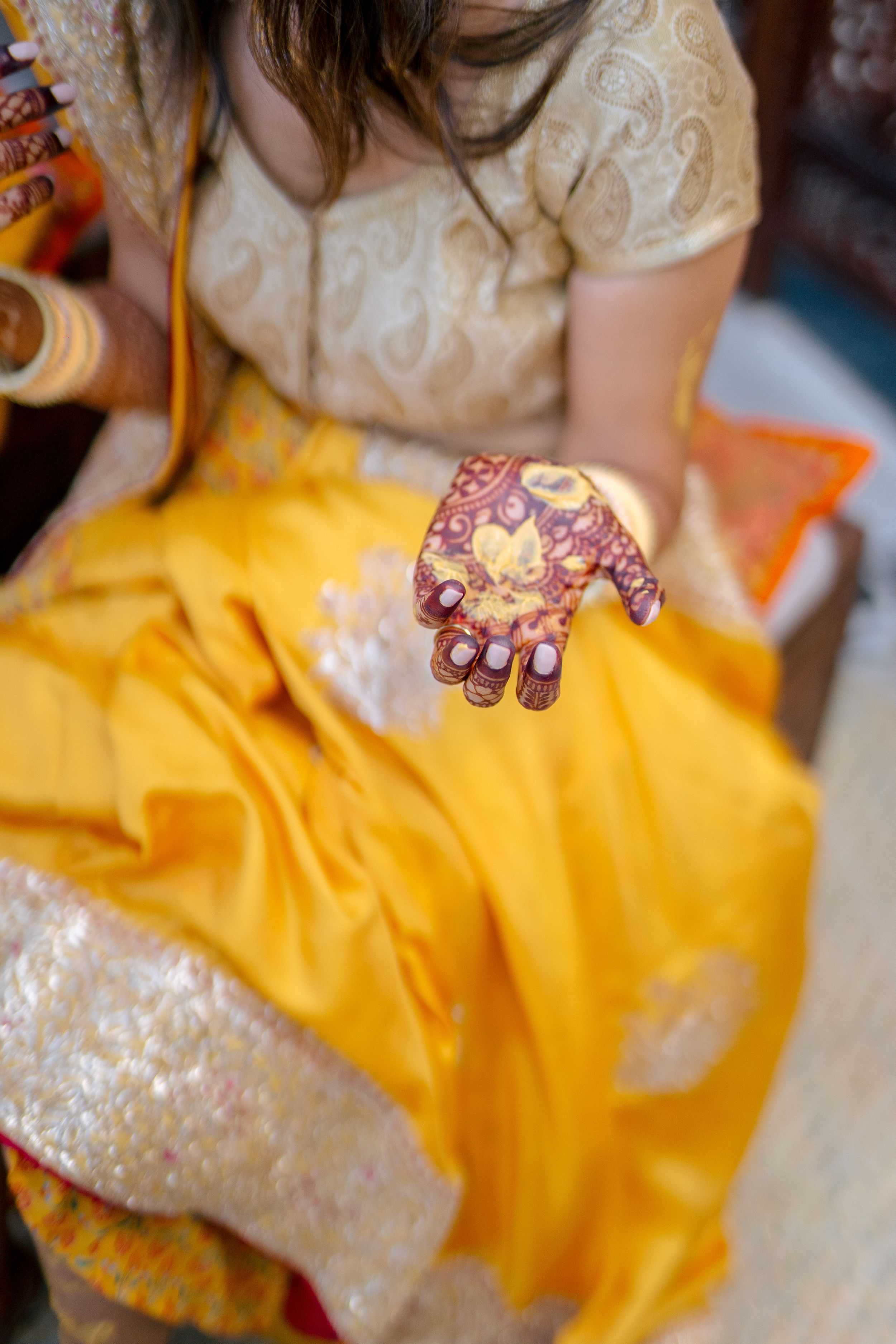 Woman in yellow lehenga displaying intricate henna mehndi design on palm during Indian wedding ceremony.