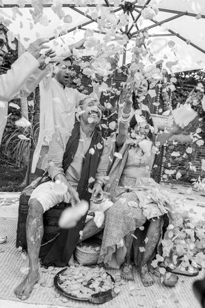 Black and white photo of a couple showered with flower petals during a traditional wedding ceremony outdoors.