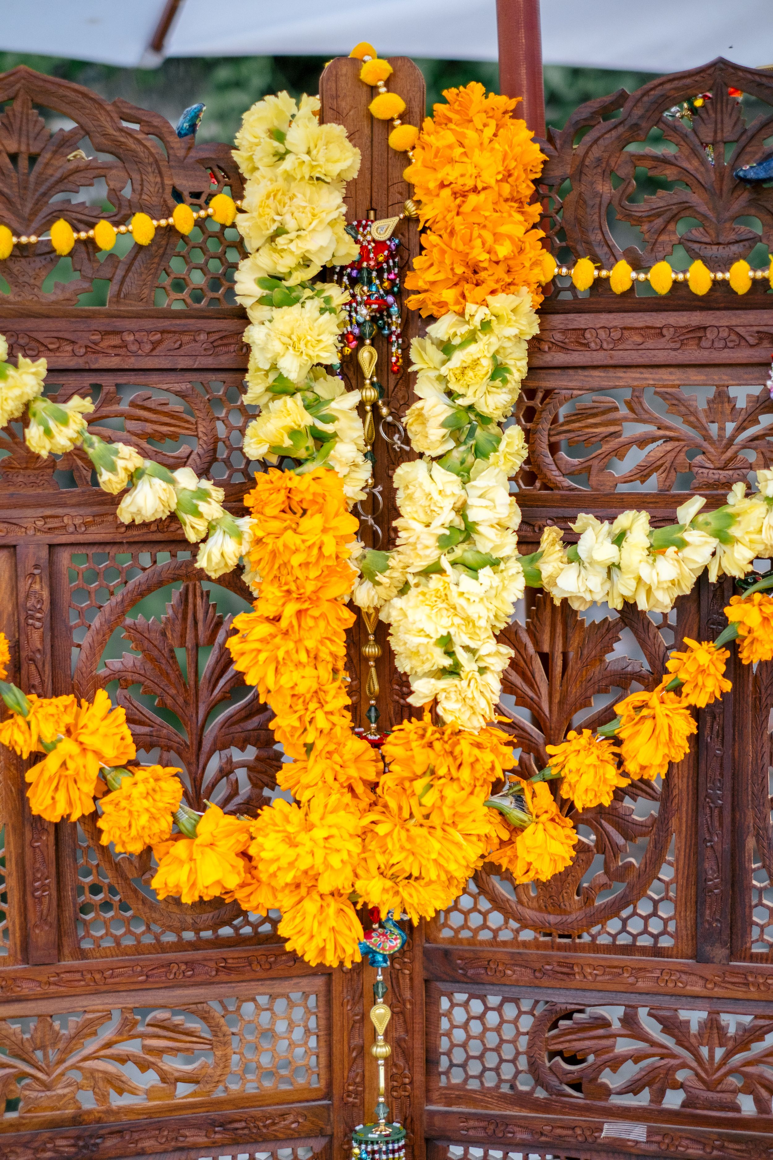 Vibrant orange and yellow marigold garlands draped on an ornate carved wooden screen for Indian festival decoration.