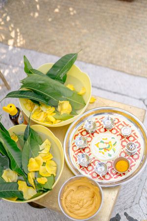 Traditional Thai Songkran ceremony items with yellow flowers, mango leaves, turmeric paste, and decorative silver bowls on a wooden tray.
