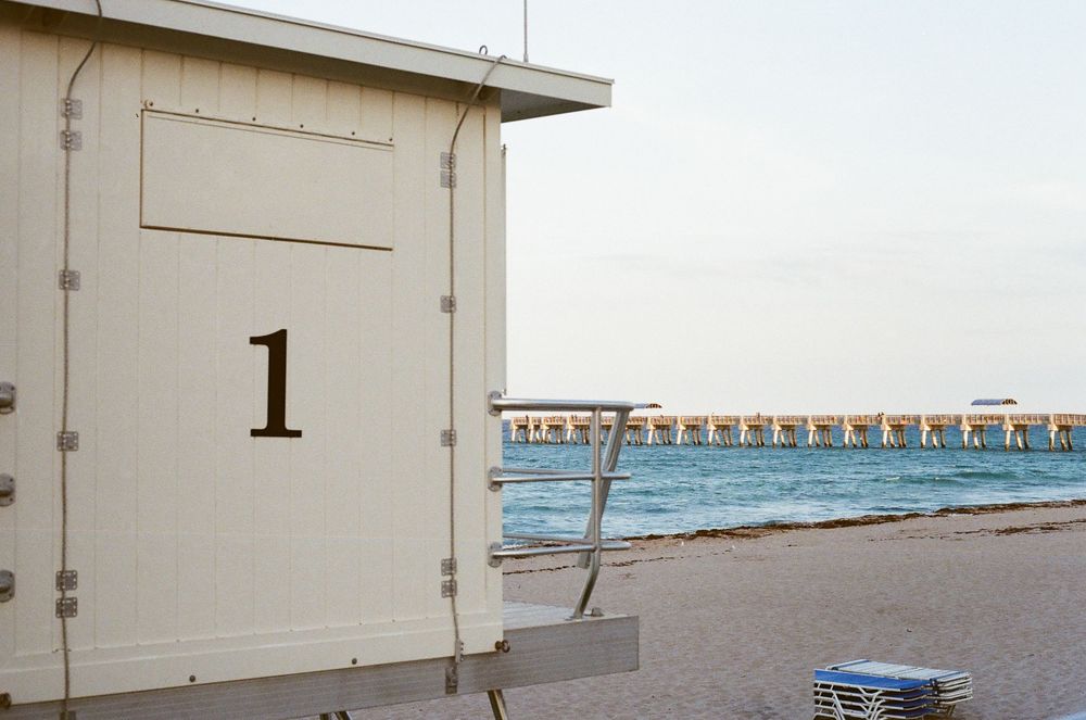 Lifeguard station number 1 on a sandy beach with a pier and calm ocean waters in the background.