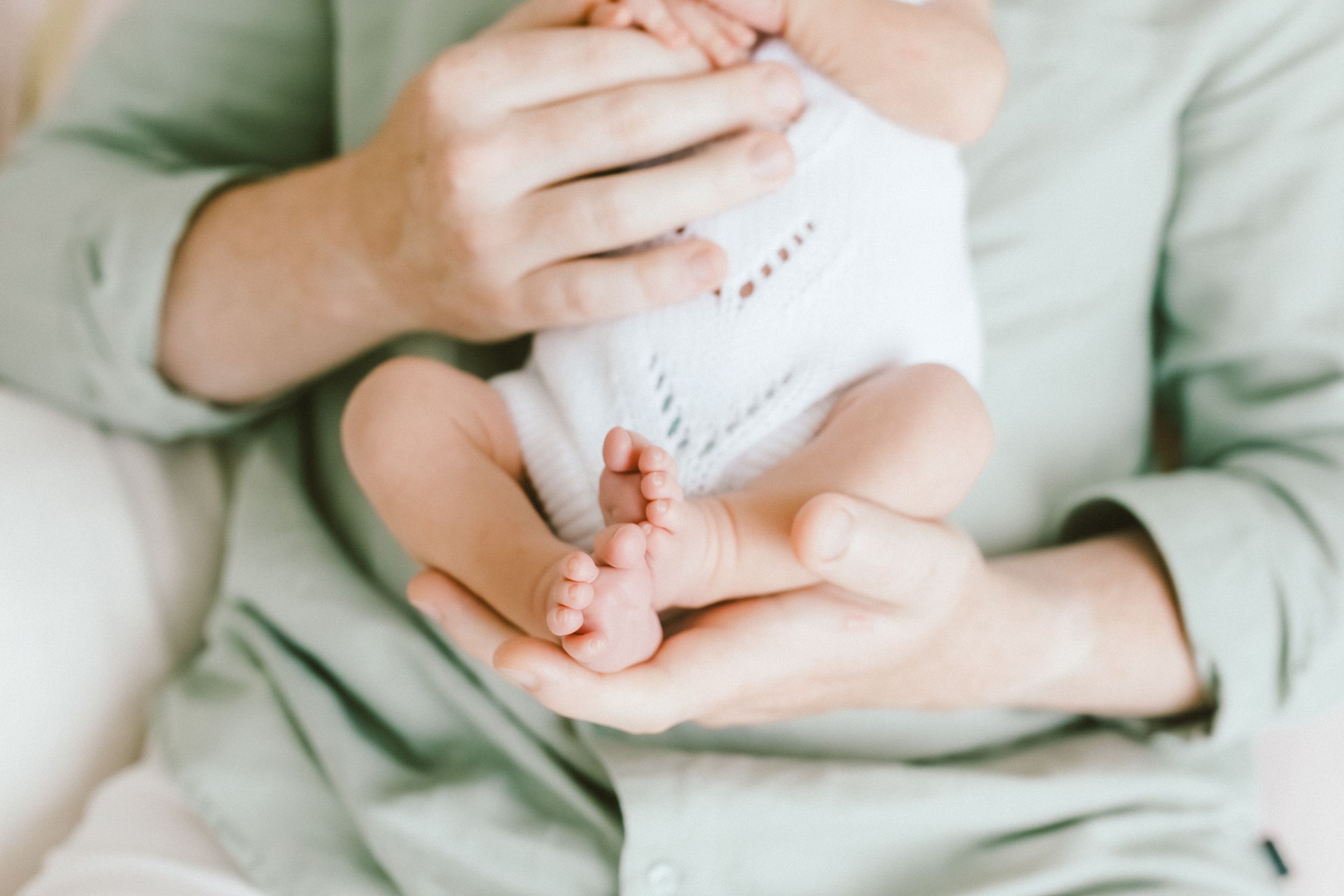 Close-up of a parent cradling a newborn baby's tiny feet in gentle hands, wearing a white onesie.