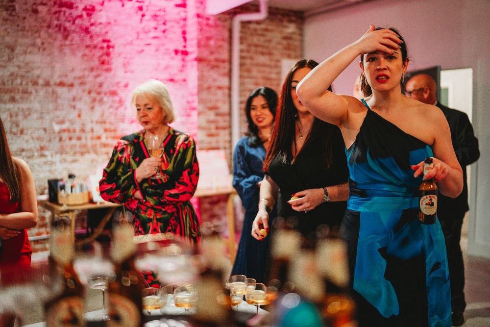 Wedding guests react emotionally during reception in industrial brick venue with pink lighting.