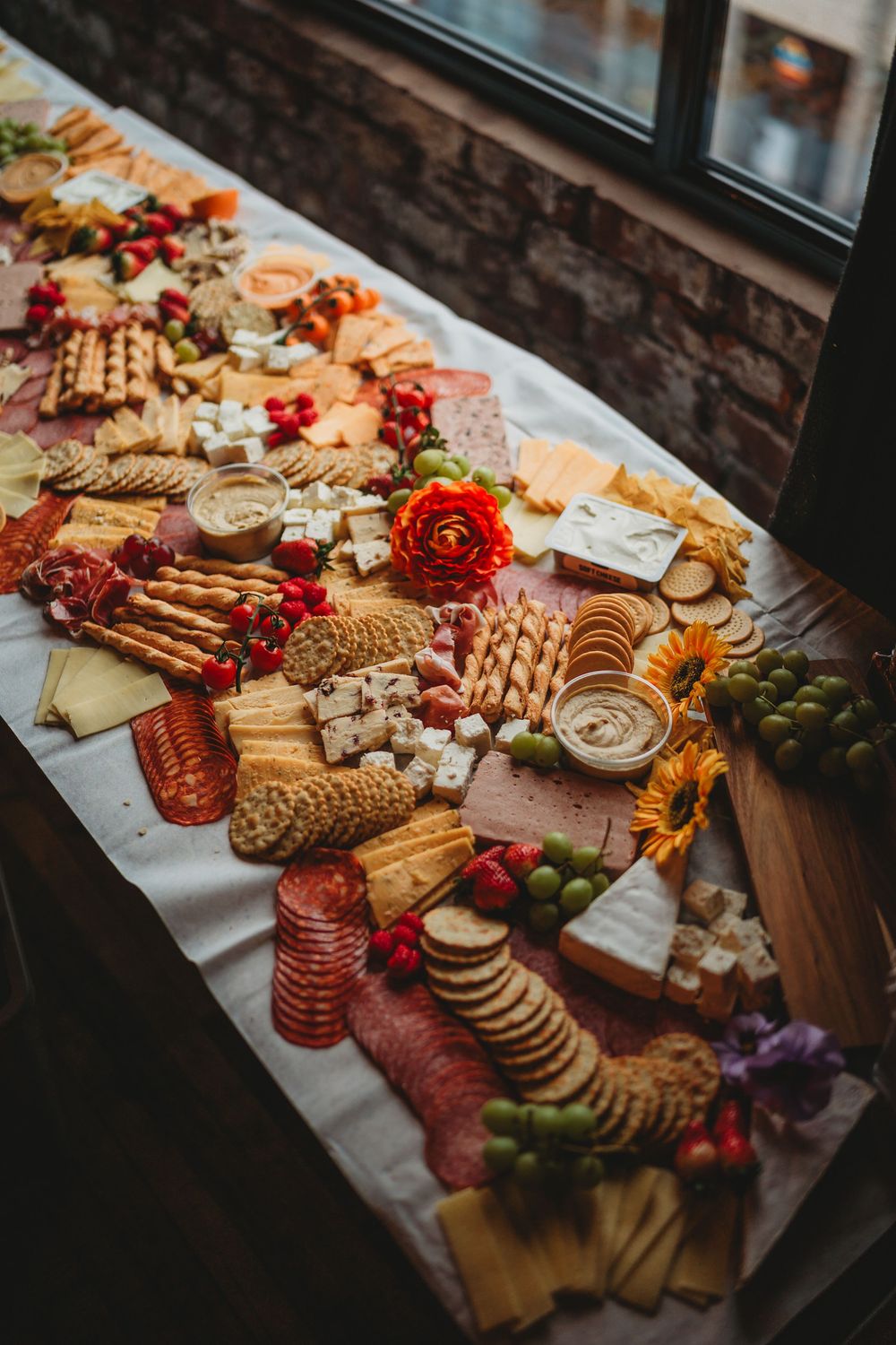 Elegant wedding charcuterie grazing table with cheeses, meats, crackers and fresh flowers.