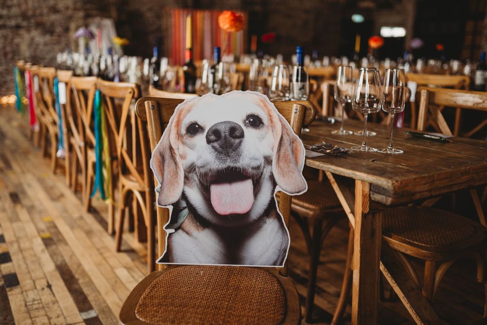 Cute dog cutout centerpiece on wooden table at rustic wedding reception venue with chairs and glassware.
