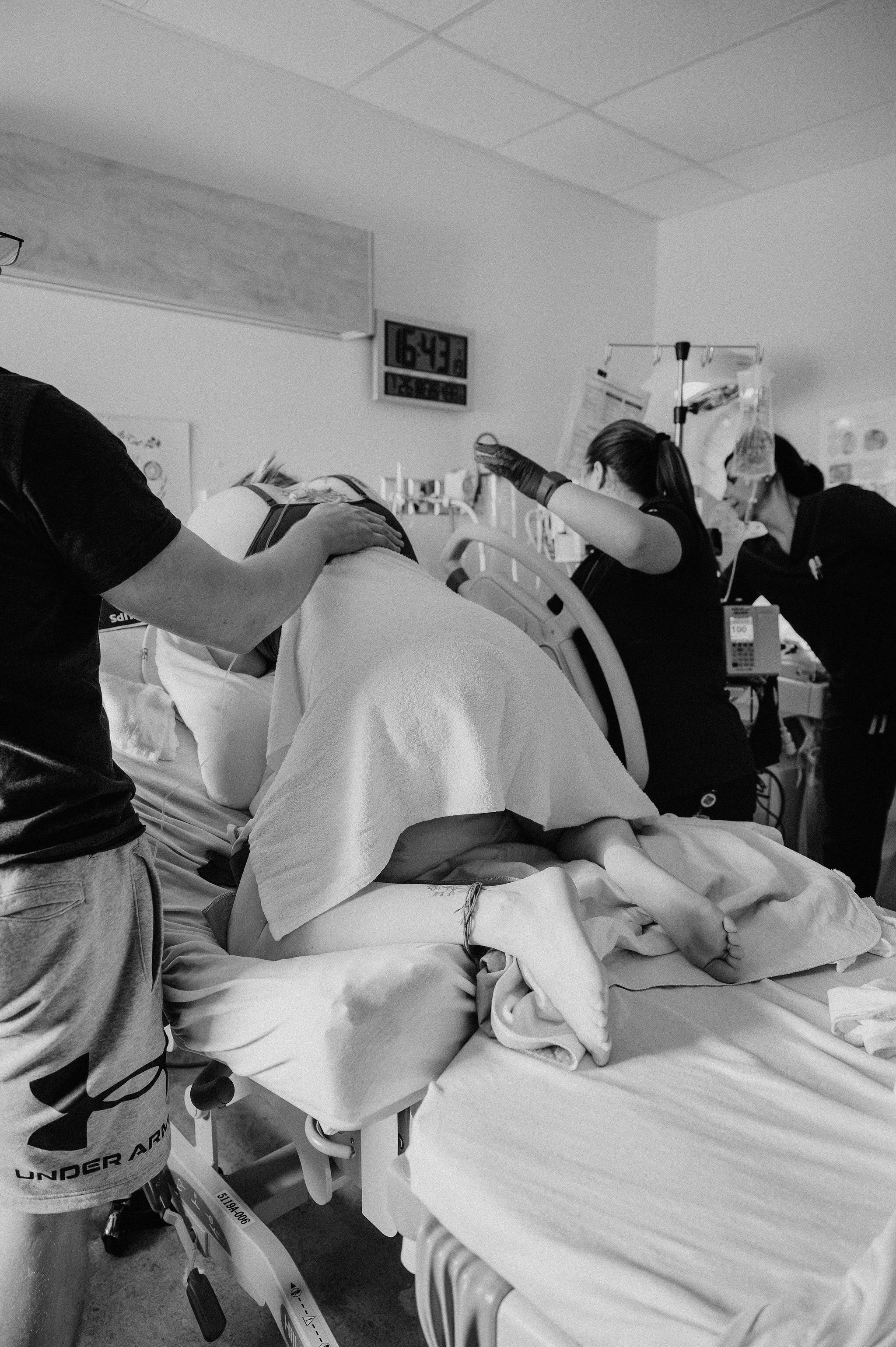 Black and white photo of medical team assisting patient in hospital bed during labor and delivery.