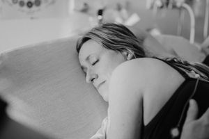 Black and white photo of a woman resting her head on a hospital bed pillow during labor.