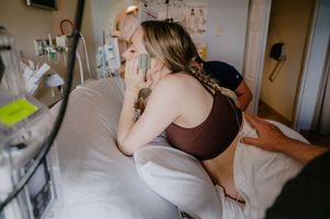 A woman in labor sitting on a hospital bed, supported by a partner during childbirth in a medical setting.