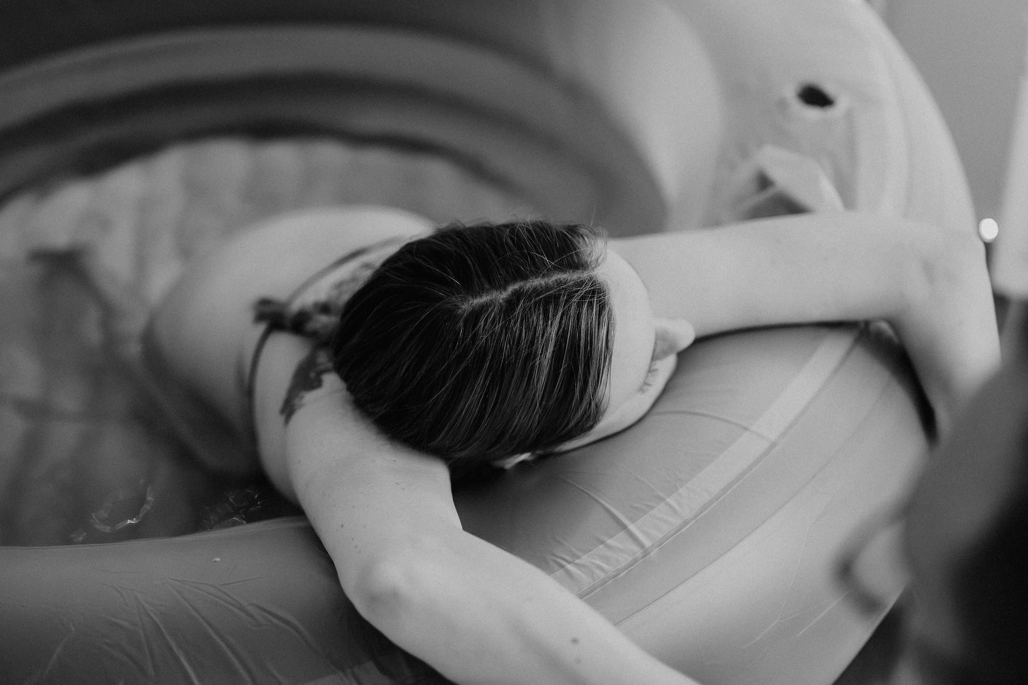 Black and white photo of a woman laboring in a birthing pool during a water birth.