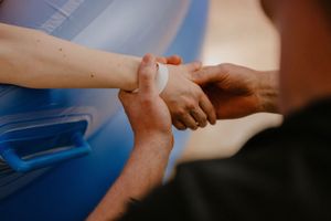 Close-up of two people shaking hands outdoors near a blue surface, one person wearing a white wrist bandage.
