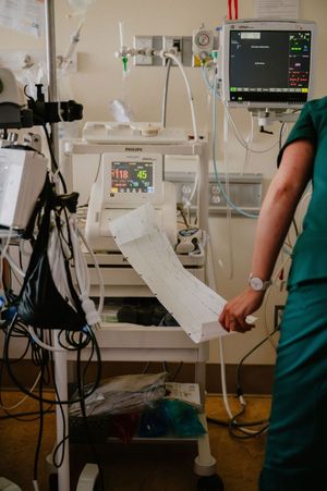 Healthcare worker in scrubs reviewing ECG printout beside Philips patient monitor in hospital ICU setting.