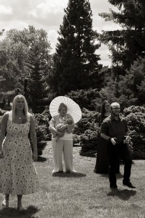 Black and white photo of wedding guests in garden, woman holding baby with white parasol centerpiece.