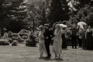 Black and white photo of wedding guests mingling on lawn with parasol visible in background.