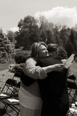 Two people sharing an emotional hug outdoors at a wedding ceremony in black and white photo.
